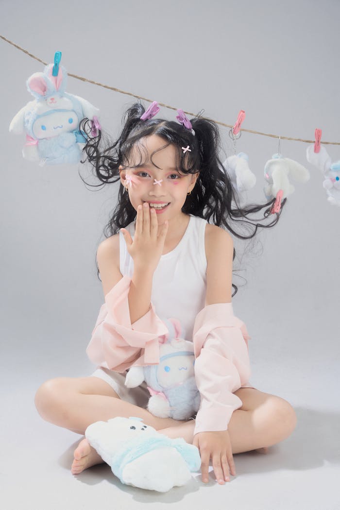 A happy girl surrounded by plush toys, smiling playfully indoors.