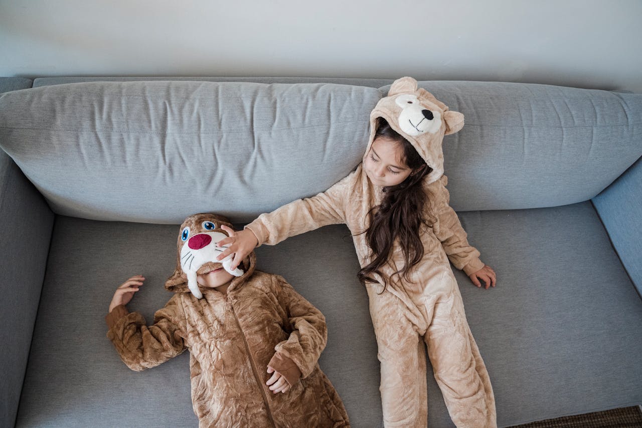 Two children in animal onesies having fun and playing on a cozy couch indoors.