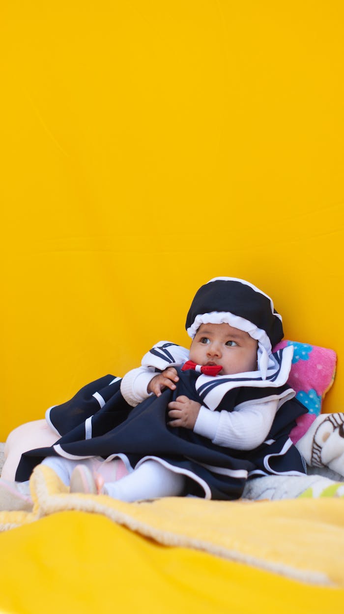 Adorable baby dressed in sailor outfit lying on colorful blankets with a vibrant yellow backdrop.